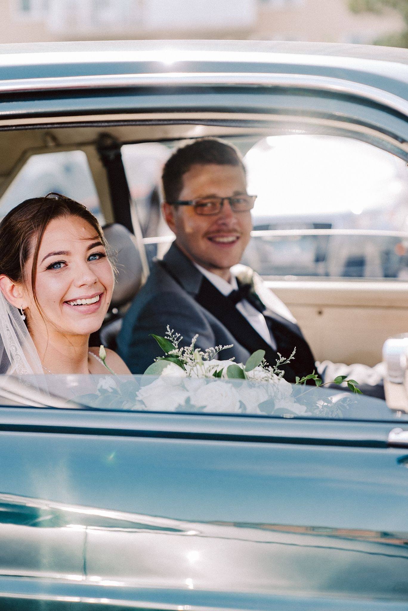Newlyweds beaming from a vintage blue car