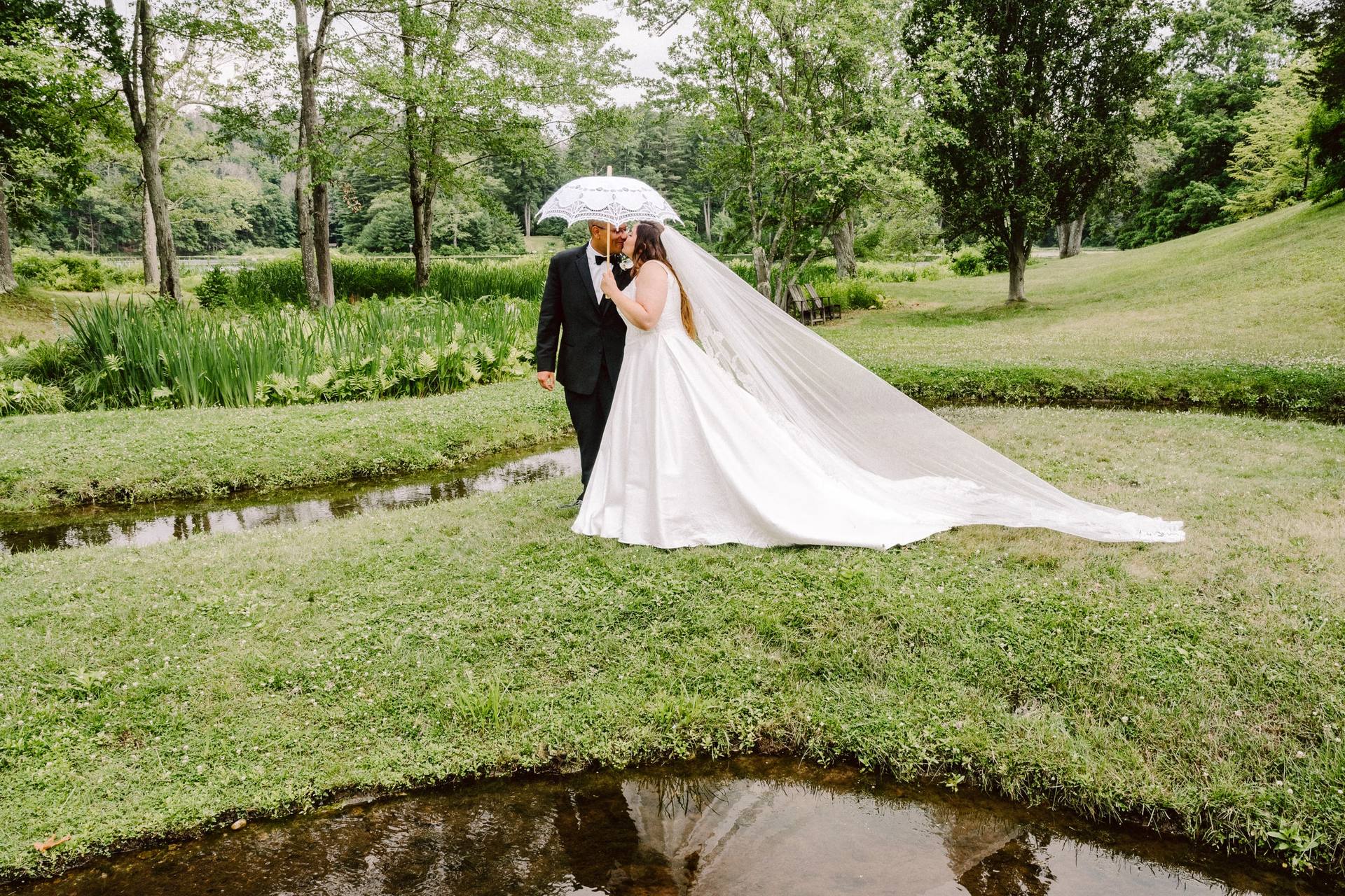 Umbrella kiss on a mossy stream bank, veil trailing