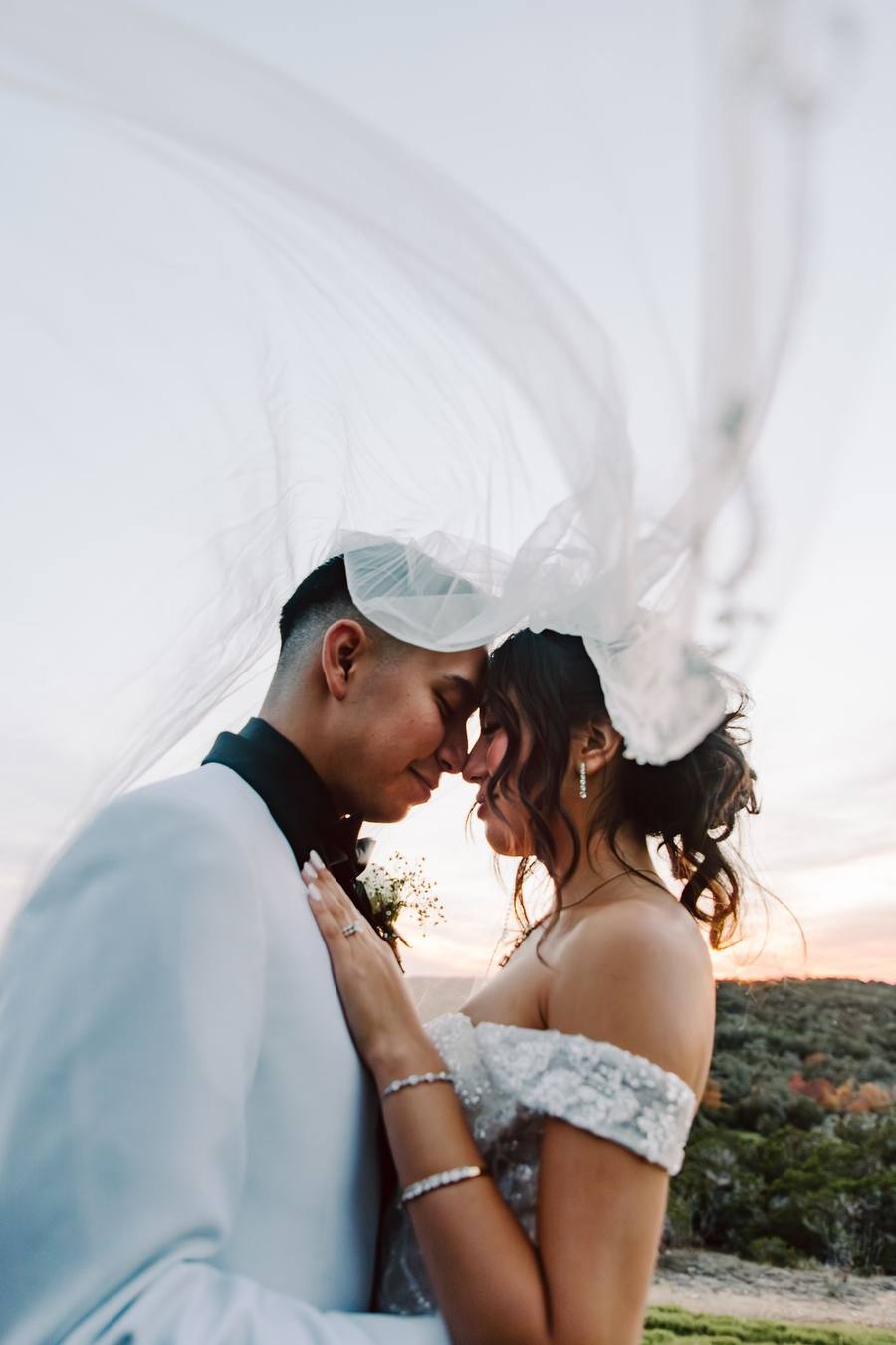 Foreheads together beneath a windswept veil at sunset