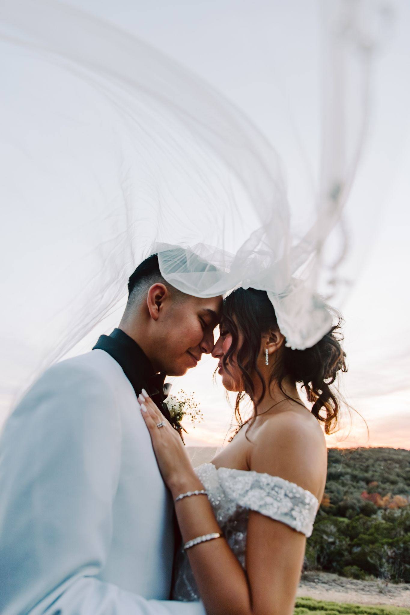 Foreheads together beneath a windswept veil at sunset