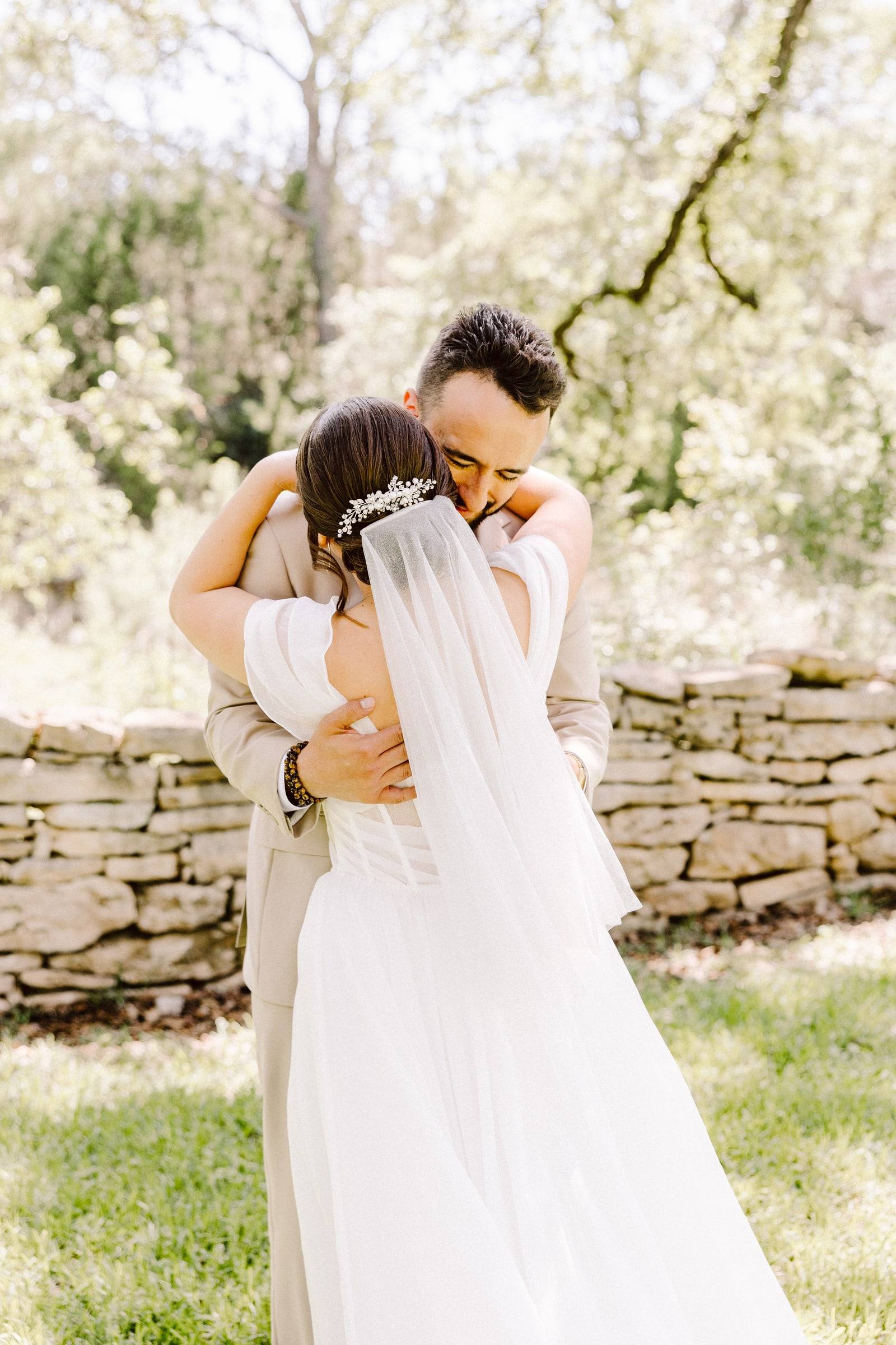 Groom embracing bride with cathedral veil at a stone wall