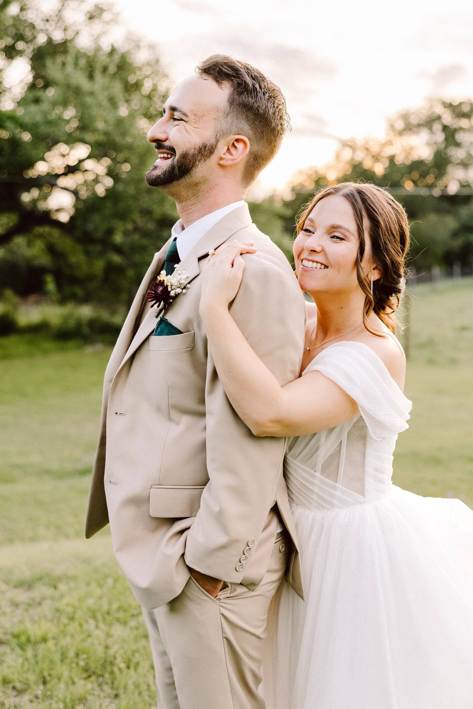 Bride hugging groom from behind at sunset