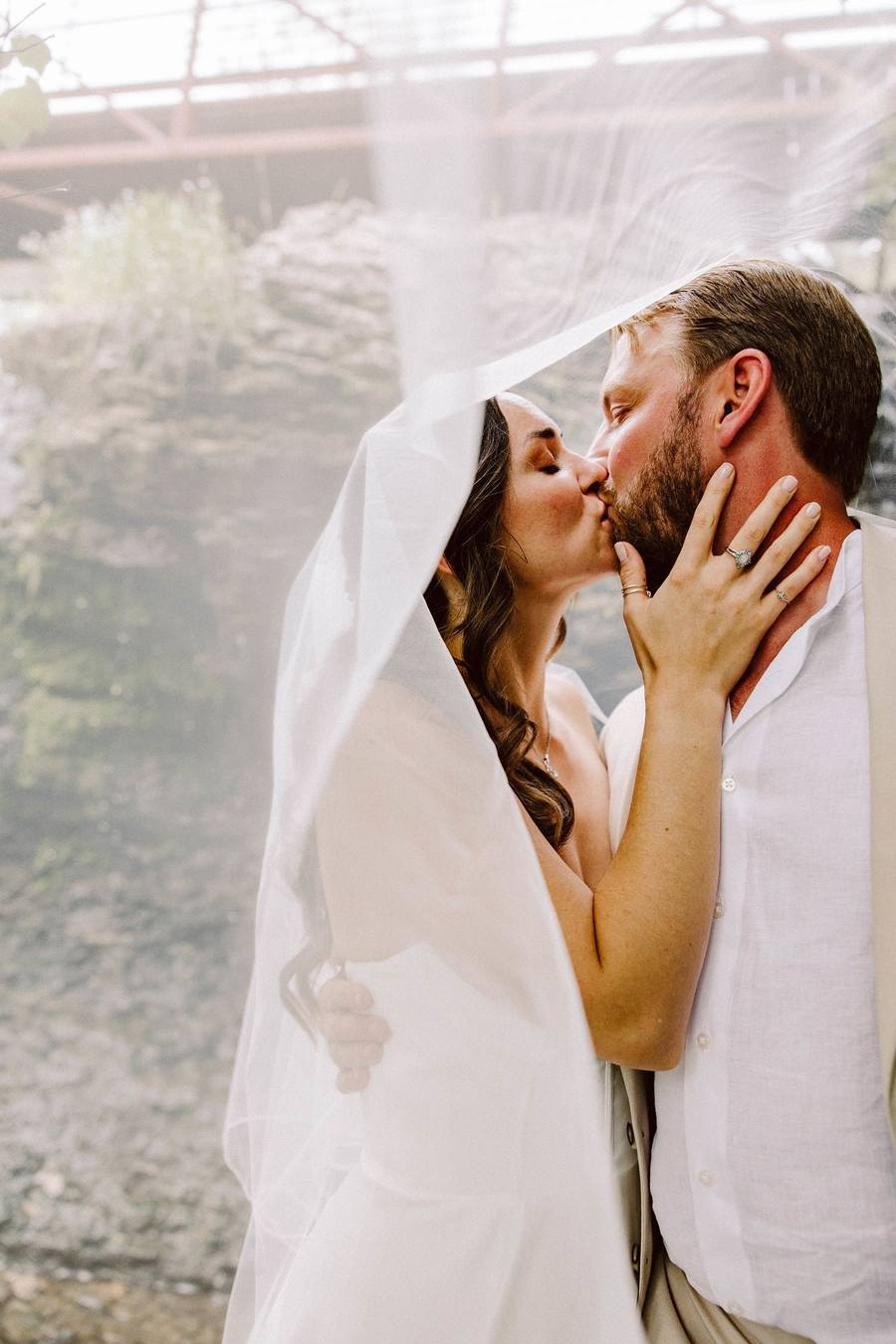 Bride and groom kissing beneath the veil by a creek
