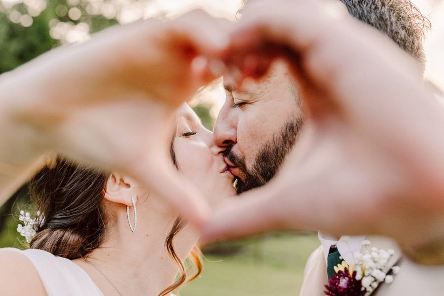 Couple kissing framed by a hand heart at golden hour