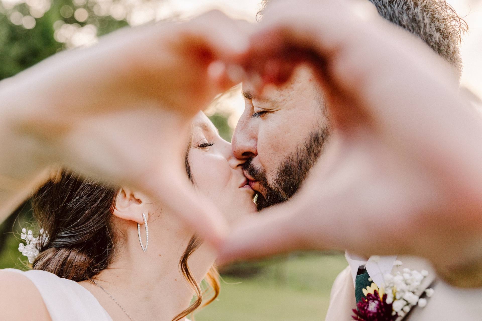 Couple kissing framed by a hand heart at golden hour