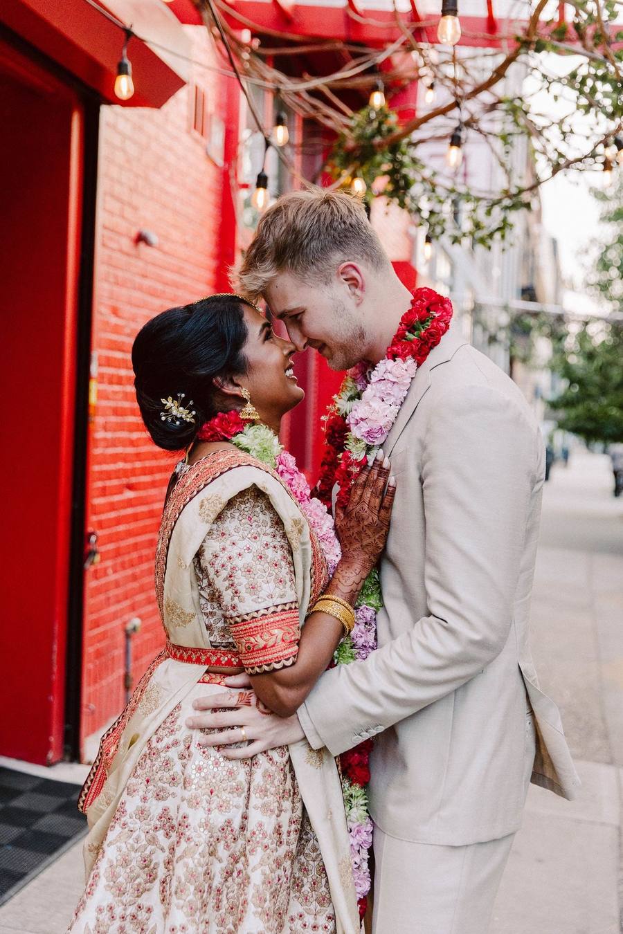 Couple in red garlands, foreheads together against a red wall