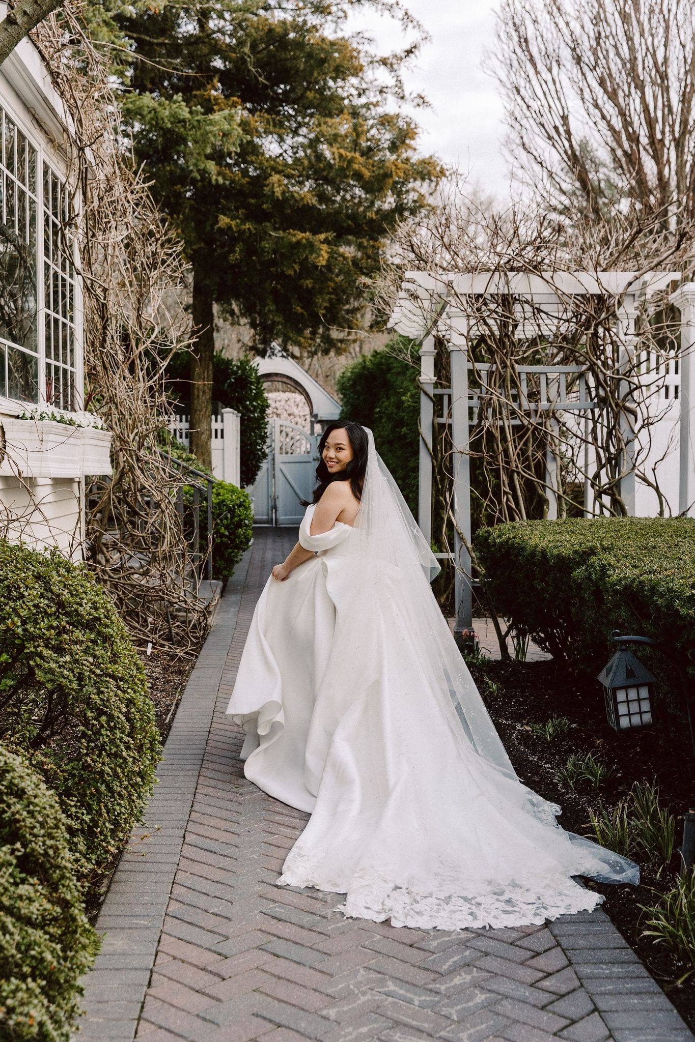 Bride glancing back on a garden path, full train