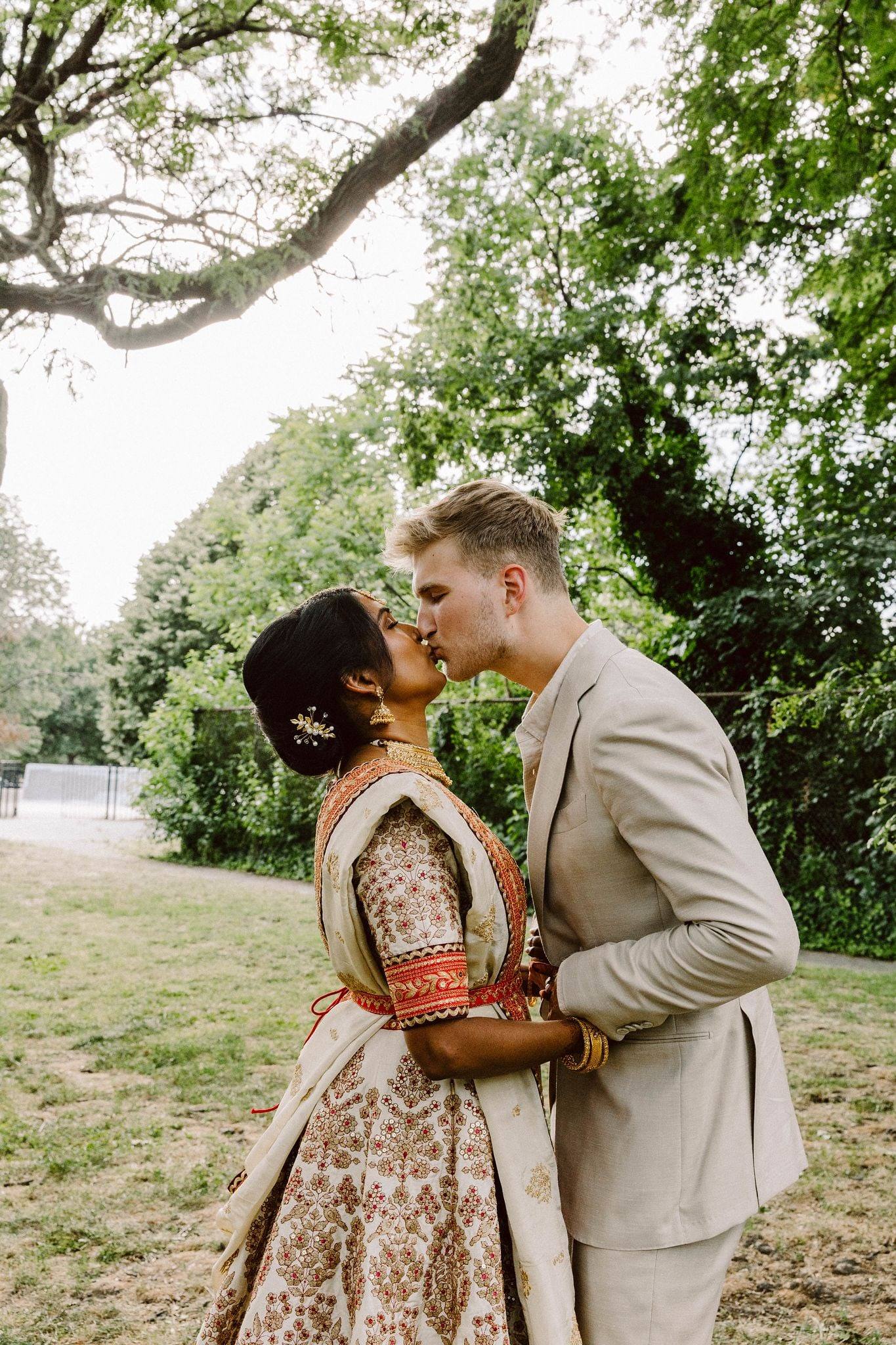 Lehenga-clad bride kissing groom beneath an oak