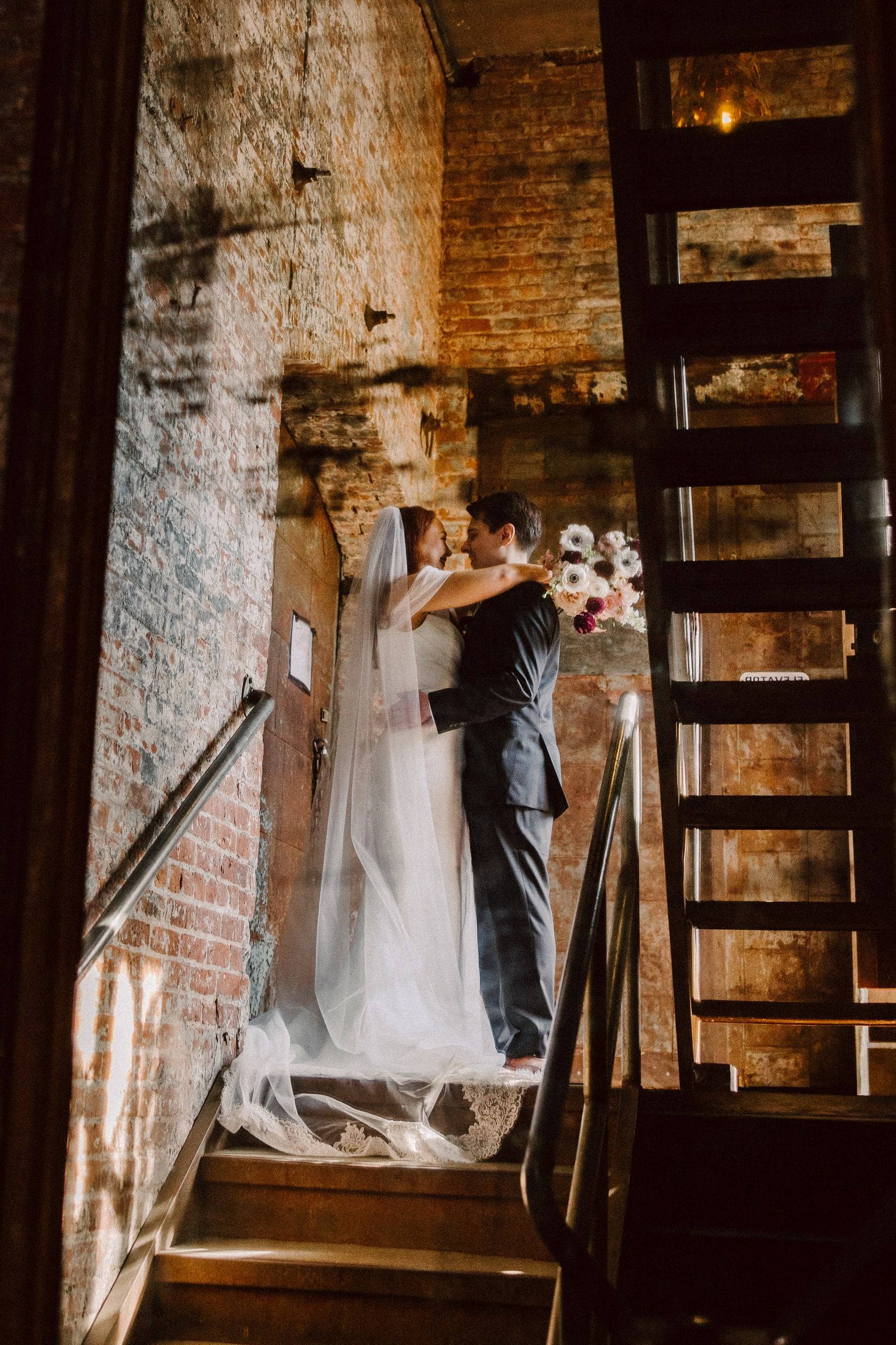 Kiss in a brick stairwell, veil catching the light