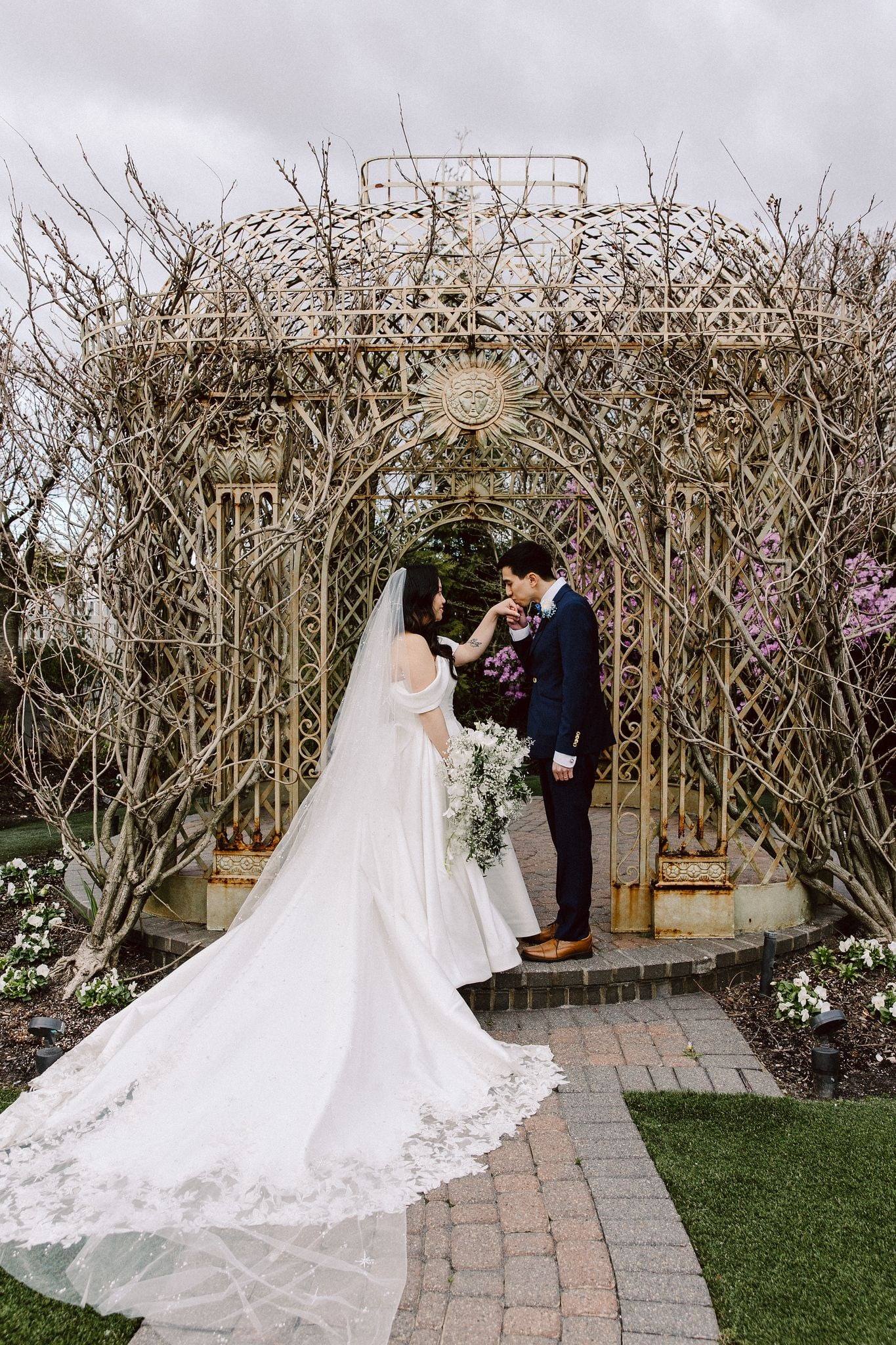 Couple at a gilded gazebo arch, train sweeping the path