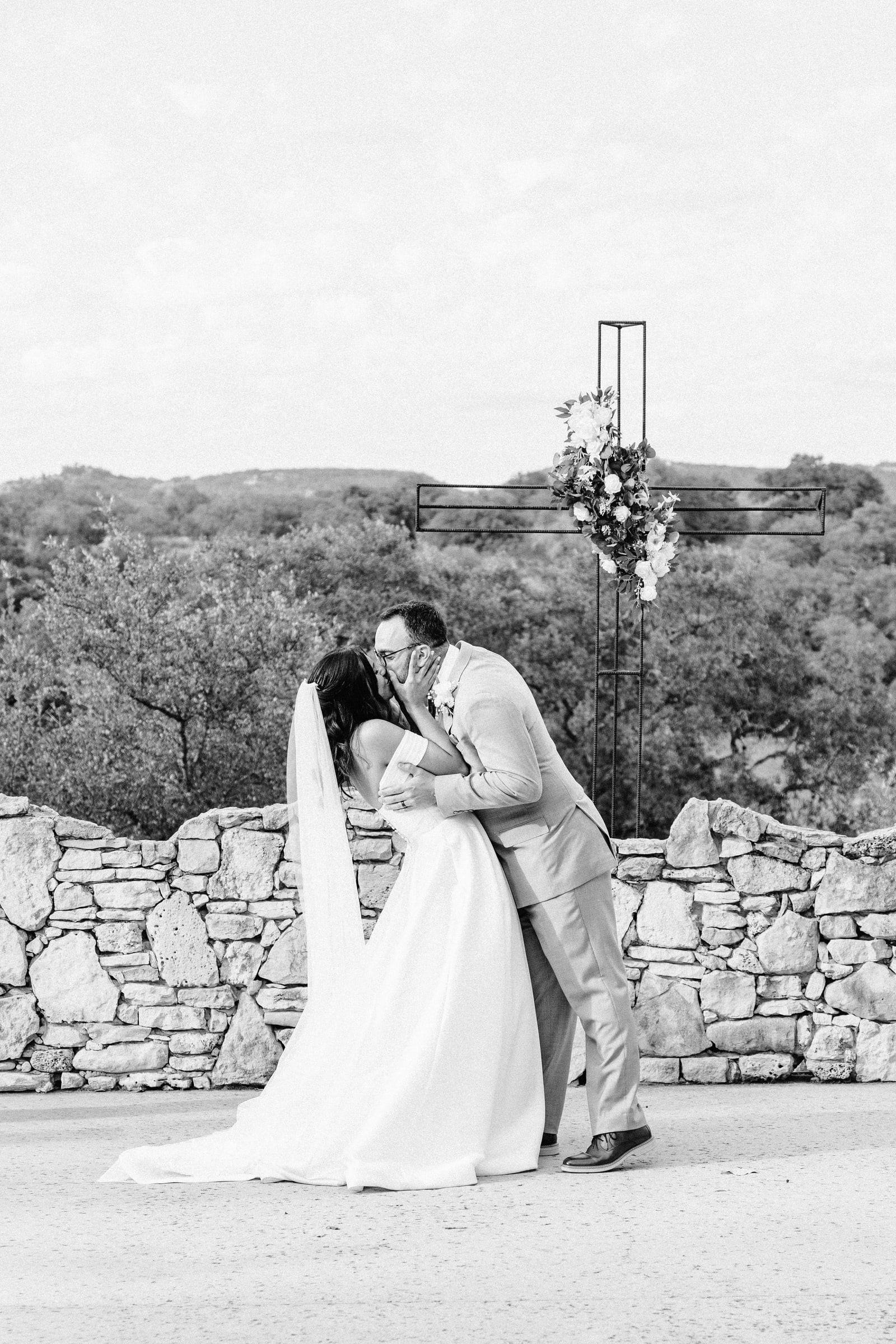 Kiss on a stone overlook by an iron cross, black and white
