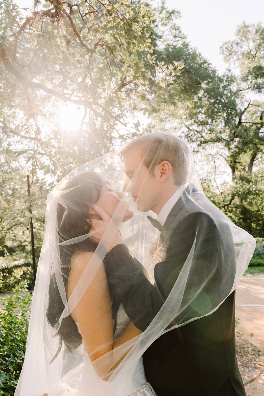 Golden-hour kiss beneath a sheer veil among oaks